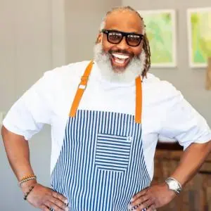 Chef Cliff Rome smiling in a white chef's coat and a blue-and-white striped apron